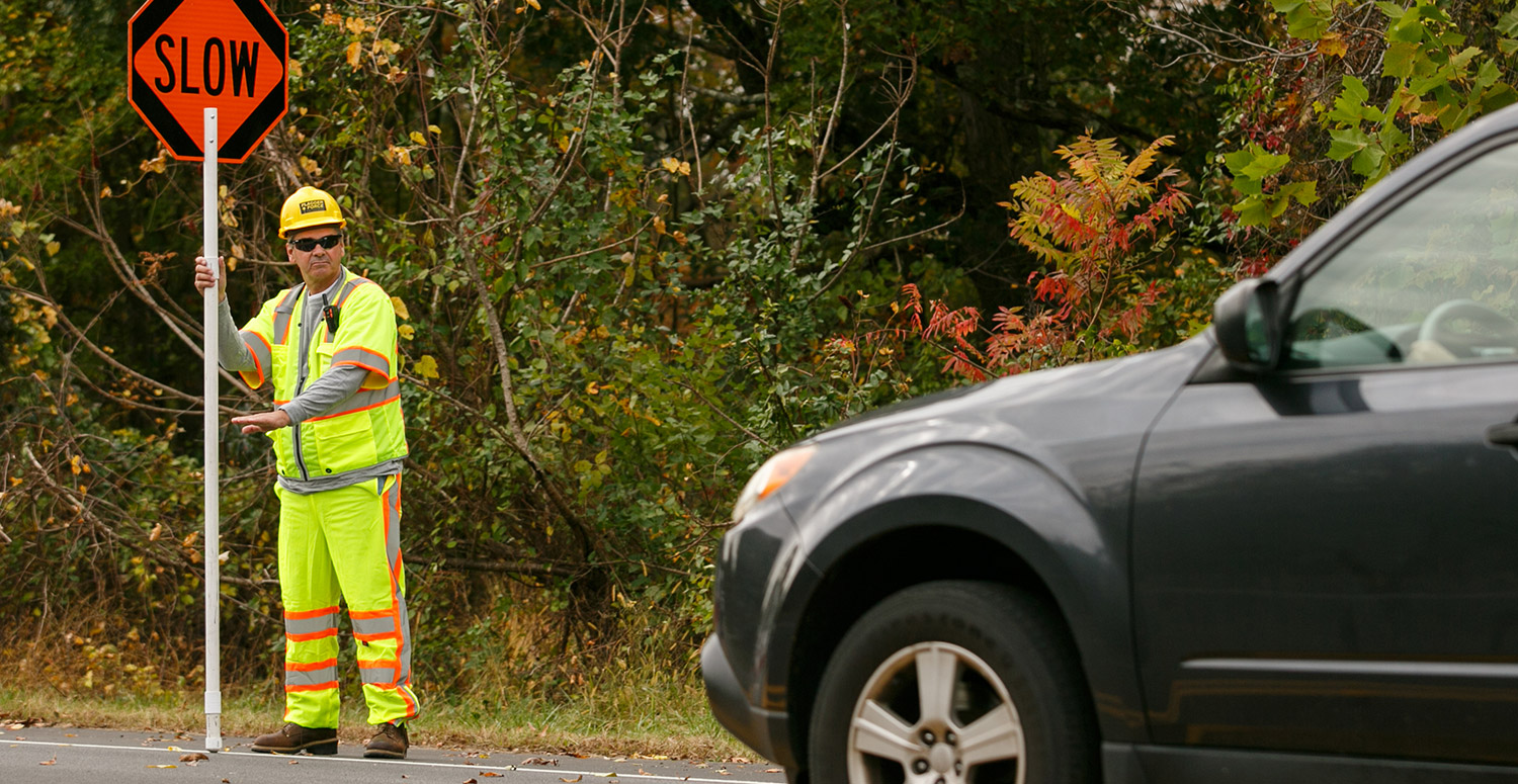 field-crew-member-holding-slow-sign-and-directing-car